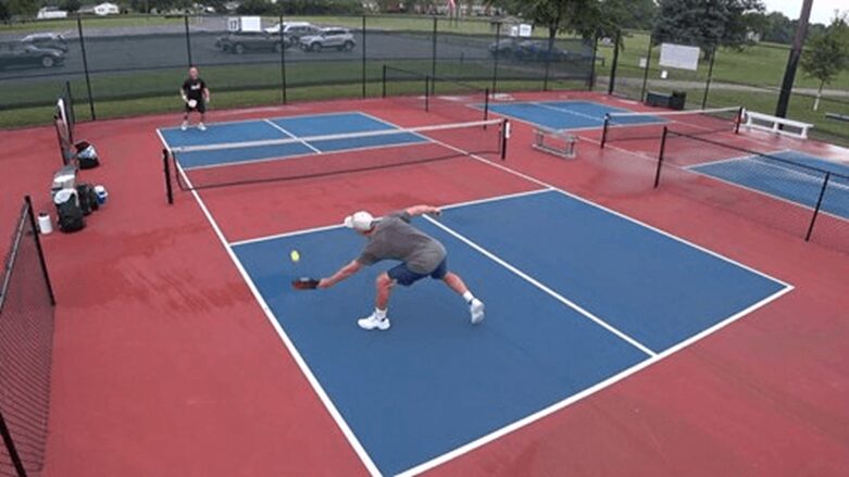 A single players plays pickleball in a court area 